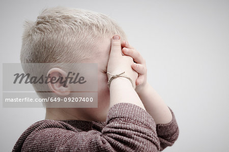 Portrait of boy wearing brown jumper, covering face with hands