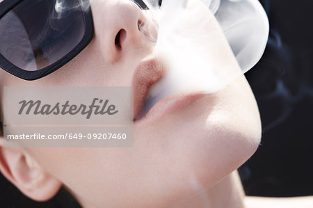 Studio head shot of young woman exhaling cigarette smoke