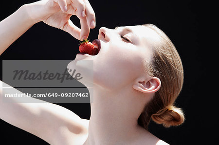 Studio shot of young woman putting strawberry into her mouth
