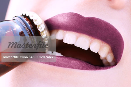 Close up young woman removing bottle top with teeth
