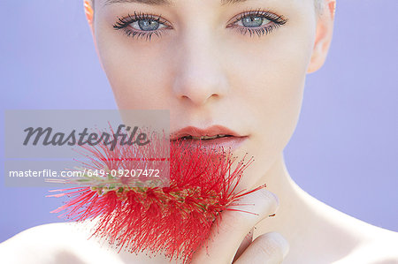 Studio head shot of young woman holding flower to her lip