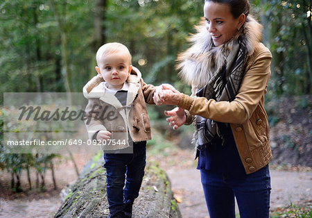 Mother walking male toddler on tree trunk