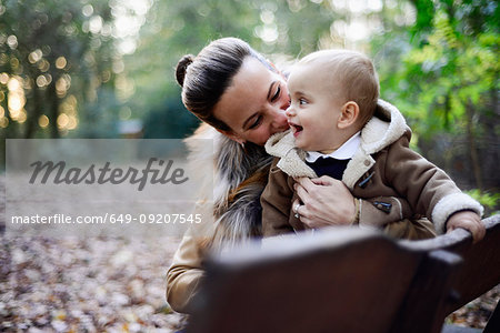 Mother holding male toddler on woodland park bench