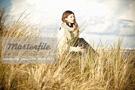 Young woman sitting in sand dunes, Bournemouth, Dorset, UK