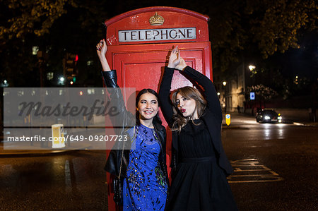 Two young female friends dancing in front of red phone box at night, London, UK