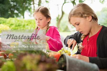 Two sisters at patio table slicing fresh fruit
