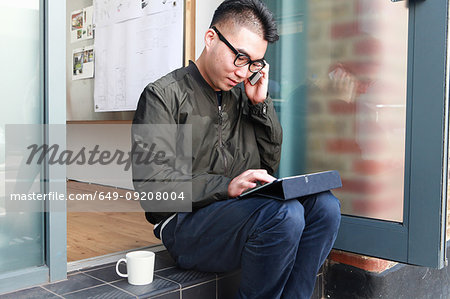 Male architect using smartphone and digital tablet on office step