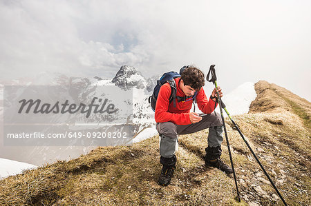 Young male mountain trekker texting on smartphone in Bavarian Alps, Oberstdorf, Bavaria, Germany