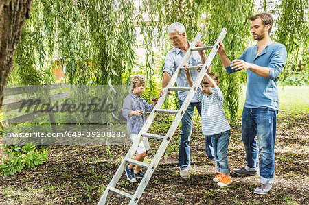 Mature man with son lifting ladder with grandsons in garden