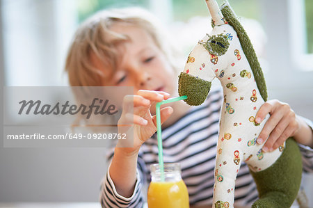 Young boy pretending to feed drink to soft toy