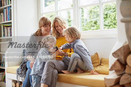 Adult women and boys sitting on window seat looking at smartphone