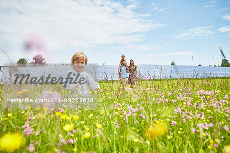 Young boy running through field, mother, father and brother following behind, next to solar farm