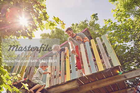 Father and two sons, painting tree house, low angle view