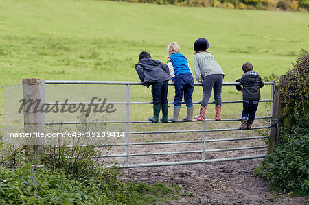 Rear view of four young children standing on gate looking out to field