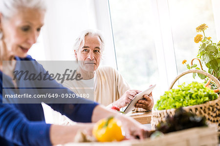 Senior couple using digital tablet and preparing food at kitchen counter