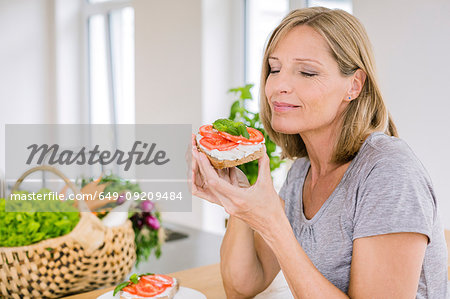 Mature woman eating open sandwich in kitchen