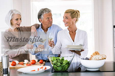 Happy senior couple and mature woman raising a glass of wine to each other in kitchen