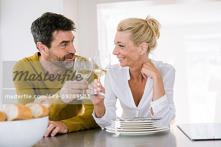 Mature couple raising a glass of wine to each other at kitchen counter