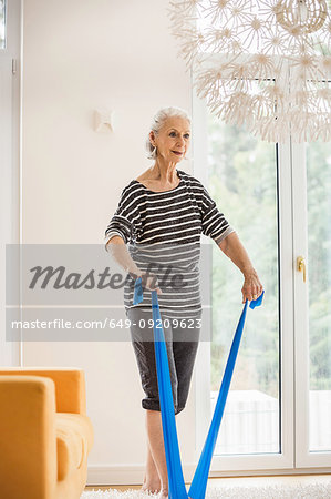 Senior woman exercising in living room pulling resistance band