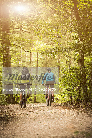 Rear view of mature mountain biking couple cycling on forest trail