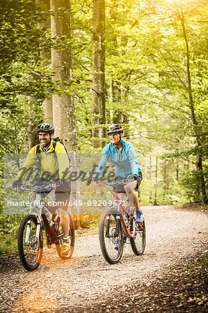 Happy mature mountain biking couple cycling on forest trail