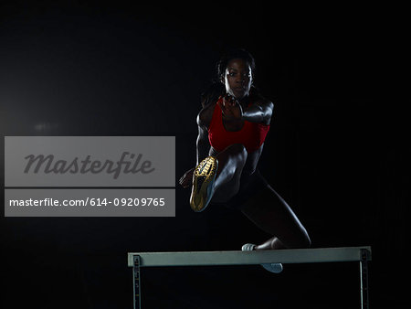 Runner jumping over hurdle on track