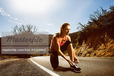 Runner lacing up shoes on rural road