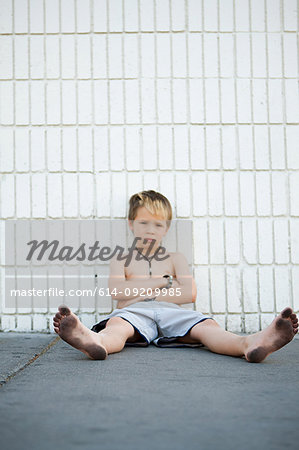 Boy with dirty feet sitting by brick wall