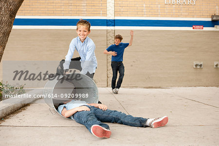 Two boys bullying another, one boy in dustbin