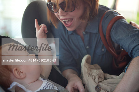 Mother putting baby daughter in car seat