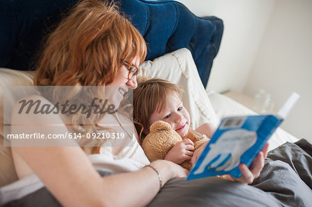 Mother and daughter reading book lying in bed