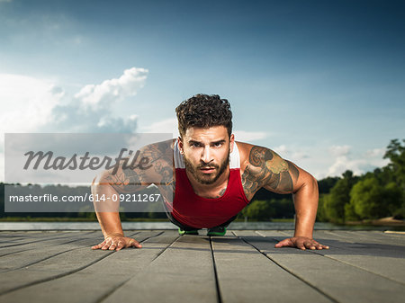 Surface level portrait of young man doing push ups on lake pier