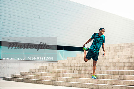 Young male runner stretching on city steps