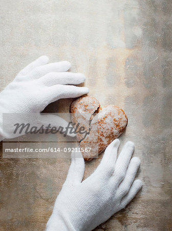 Gloved hands holding heart-shaped gingerbread cookie