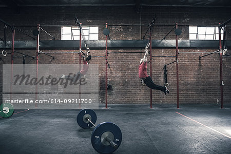 Young male and female crossfitter swinging on gym rings in gym