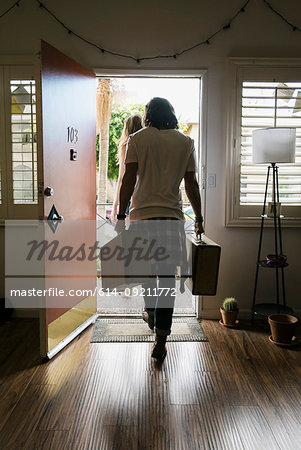 Rear view of young couple carrying suitcases out of front door