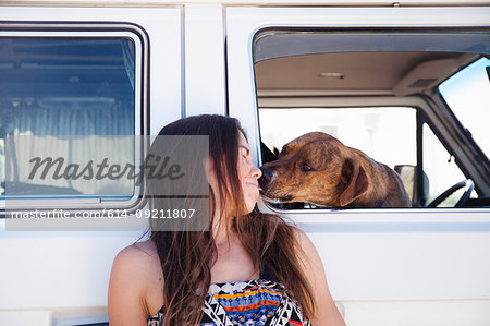 Pet dog inside camper van, reaching out to lick face of woman beside van