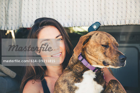 Woman sitting in camper van hugging pet dog
