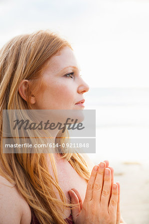 Close up of mid adult woman practicing yoga with hands together on beach