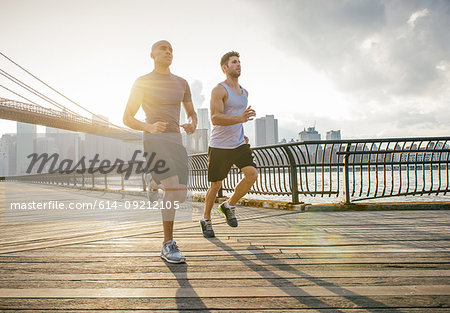 Two male running friends running in front of Brooklyn bridge, New York, USA