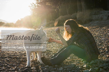 Woman sitting on bank of Bitterroot River stroking dog smiling, Missoula, Montana, USA