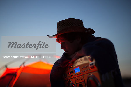 Side view of teenage boy in silhouette wearing hat, holding boom box