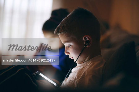 Side view of boy on sofa wearing earphones looking down using digital tablet