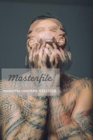 Multiple exposure of bare chested young man, covered in tattoos, screaming