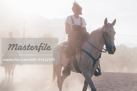 Cool young man riding horse in dusty rural equestrian arena