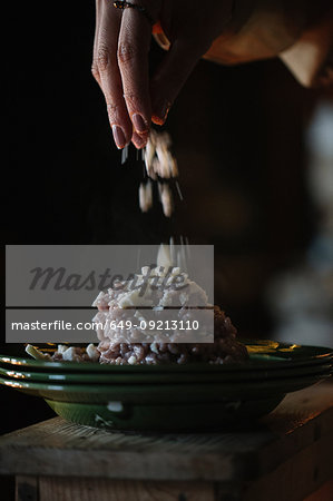 Young woman adding garnish to bowl of risotto, close up of hand