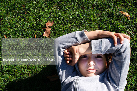 Boy on grass blocking sunlight with arms