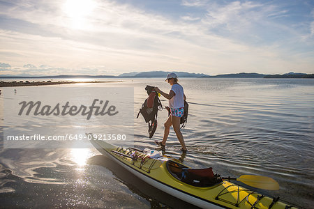 Mature female kayaker carrying life jackets from kayak, Quadra Island, Campbell River, Canada