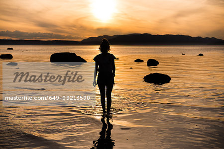 Young woman looking out at sunset, silhouetted rear view, Quadra Island, Campbell River, Canada