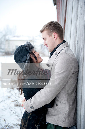 Young couple hugging against cabin in snow